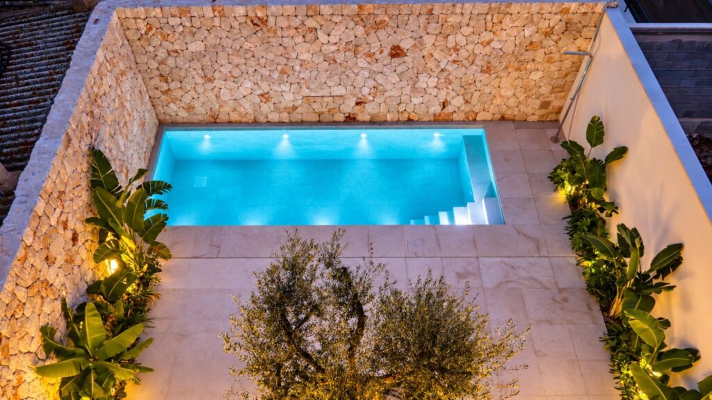 Vista cenital de la piscina salina del patio, rodeada de muro de piedra y vegetación mediterránea